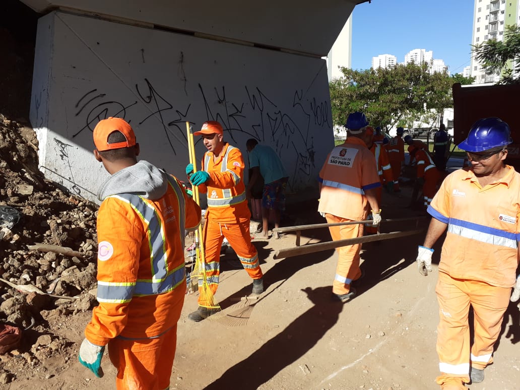 Pessoas com uniforme padrão laranja limpando de baixo do viaduto